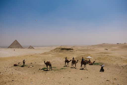 A group of camels and people take a break from their journey amongst the majestic pyramids in the Sahara desert