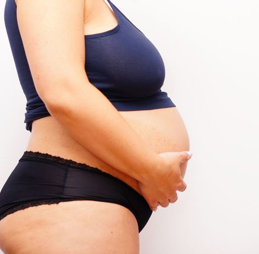 A closeup of a pregnant woman holding her belly under the lights against a white background