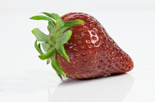 A red strawberry resting on a plain white surface, illuminated by a light source