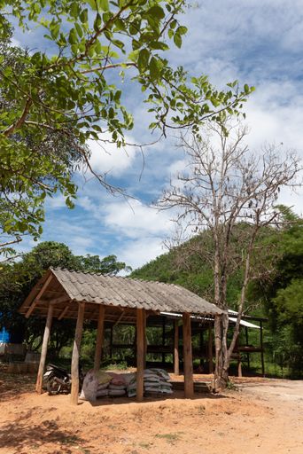 A vertical shot of a wooden hut in a sunny rural area in Western Thailand