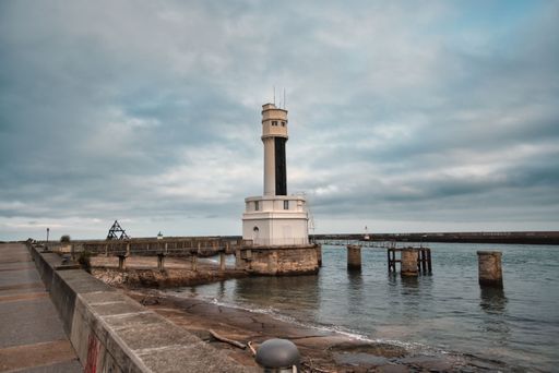 A lighthouse standing tall in a tranquil sea, with a cloudy sky in the background