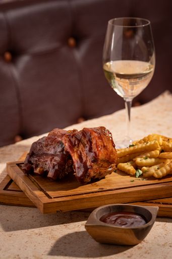 A cozy outdoor dining setup with savory meat, fries and a glass of wine