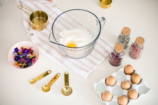 A bowl filled with fresh eggs and flour surrounded by cooking utensils on a white surface