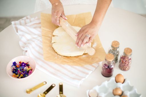 A young adult rolling out dough in the kitchen surrounded by ingredients