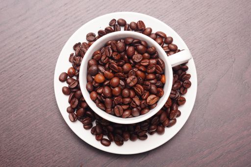 A beautiful shot of coffee beans in the white cup and plate on a wooden table