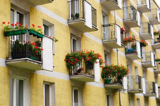 A vertical shot of the balconies with metal fences of a yellow building with a dog sitting in one