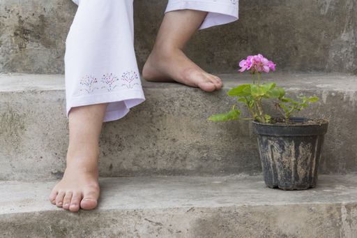 A woman's bare feet with a pink geranium on a pot in the stairs