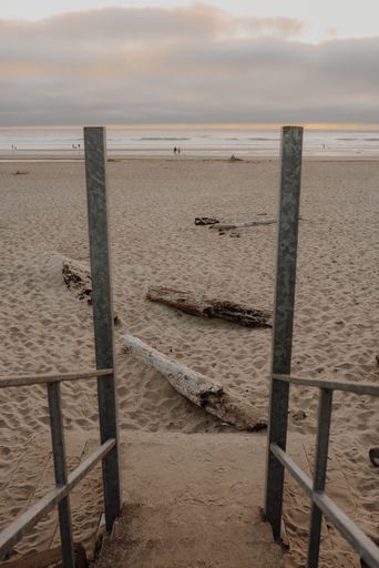 A vertical picture of a beach surrounded by the sea under a cloudy sky during the sunset