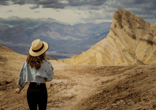 A shallow focus of a young woman with a fedora hat hiking in a deserted area