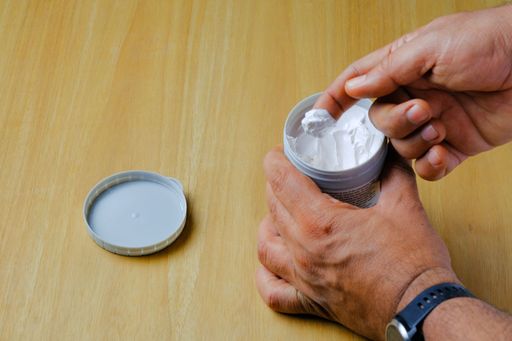 A closeup shot of hands of a man taking ointment by finger from a plastic can on wooden surface