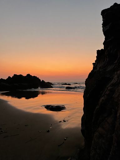 A vertical of a rocky cliff overlooking a sandy beach at sunset