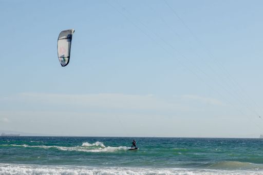 A Hispanic young man doing kitesurfing with foamy waves in Tarifa, Spain on a sunny day
