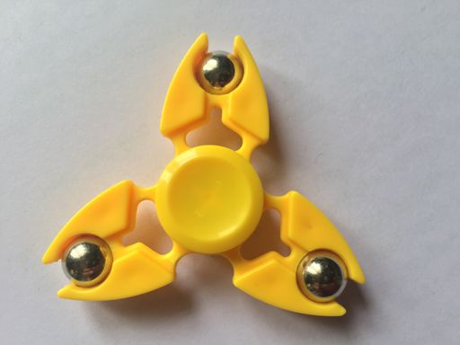 A closeup of a plastic yellow fidget spinner on a white surface