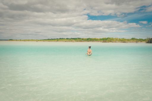 A woman go to swim through turquoise colors of the lagoon of bacalar in Mexico