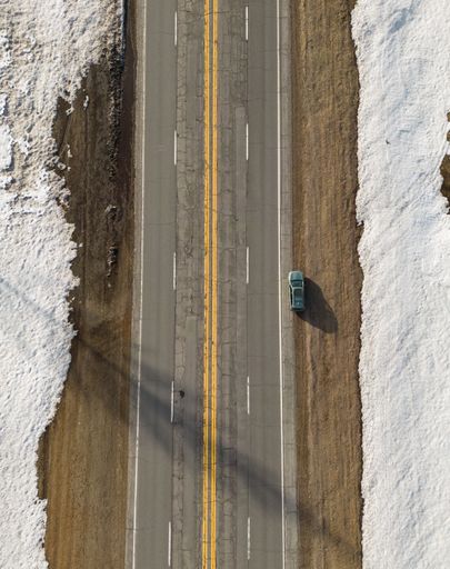 An aerial view of a car driving along a road through a snowy winter landscape