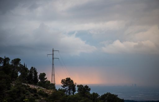 A hill covered in greenery surrounded by the sea under a cloudy sky during the evening