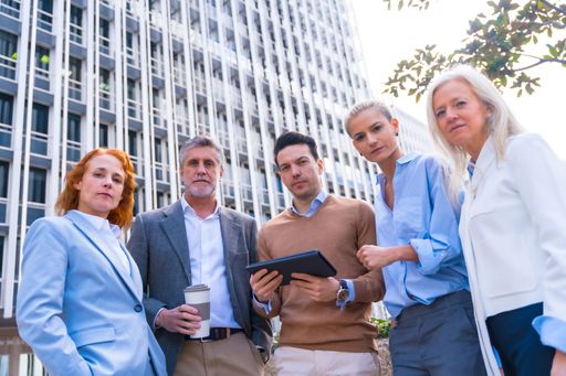 Five business professionals gathered around a tablet, discussing a project and looking at the camera