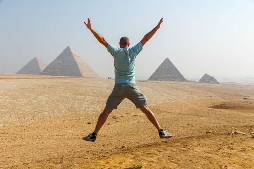 A rear view of a man jumping against the famous pyramids of Giza in Egypt