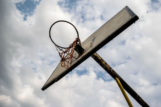 A low angle shot of a rusty old basketball hoop under a cloudy blue sky