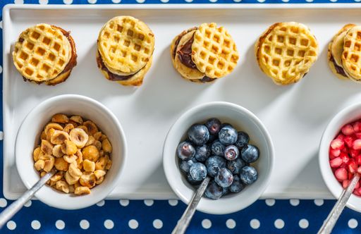 A top view of bowls of breakfast food with waffles, blueberries, granola