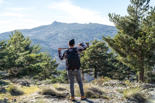 A Spanish Lumberjack man with backpack and ax on his shoulder walking up the mountain