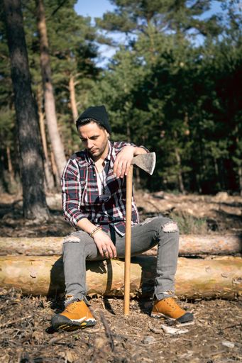 A thoughtful lumberman is resting on a wooden log g leaning on his ax