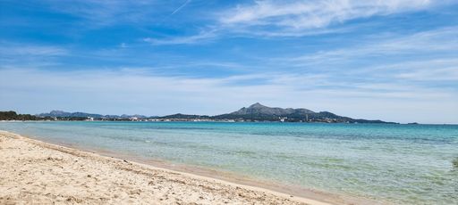The sandy beach and crystal clear, blue waters lapping against the shore. Alcudia, Balearic Islands.