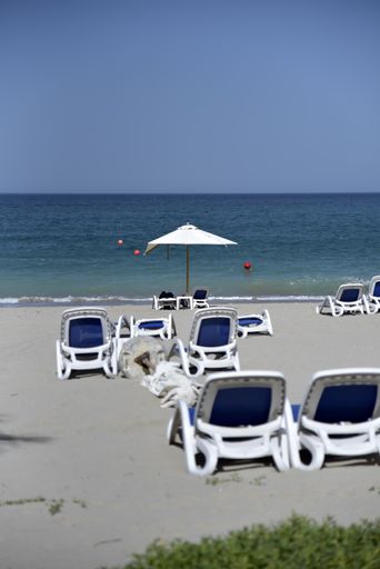 A vertical shot of  sandy beach with deck chairs and one beach umbrella