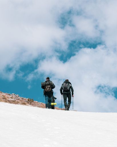 Two friends having an outdoor winter adventure, walking down a snow-covered hillside, enjoying the scenery