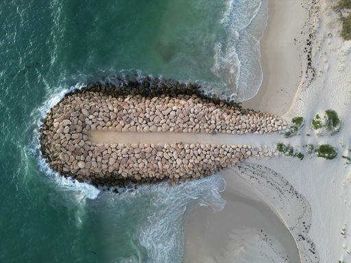 An aerial shot of a beach, featuring rocks and crystal-clear blue water