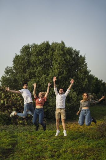 A vertical shot of Spanish Caucasian young friends jumping happily in a park