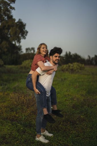 A vertical shot of a Spanish Caucasian couple in the park, him giving her a piggyback ride