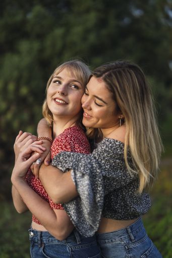 A vertical shot of two beautiful Spanish Caucasian friends hugging lovingly in the park