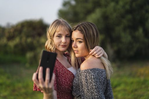 A shallow focus shot of two beautiful Spanish Caucasian friends hugging, taking a selfie in the park