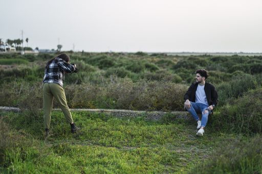 A closeup of a female photographer taking a photo of a Spanish Caucasian man, in a park