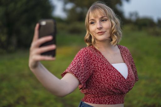 A shallow focus shot of a beautiful blonde Spanish Caucasian woman taking a selfie in the park