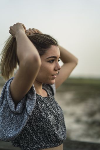 A vertical shot of a beautiful Spanish Caucasian young woman fixing her hair in the park