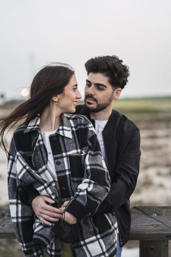 A vertical shot of a cute Spanish Caucasian couple gazing at each other lovingly, outdoors