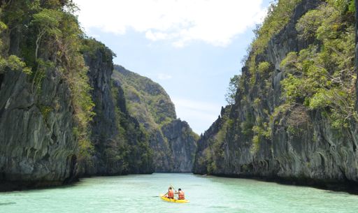 A wide shot of two males rowing a boat in life vests on beautiful El Nido island in the Philippines