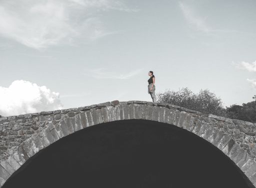 A woman standing on an old arch brick bridge against a cloudy sky - decision making concept