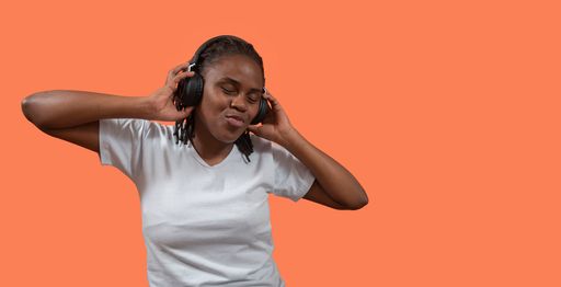 happy African young woman listening to music on headphones, eyes closed and holding headphones with hands, dressed in white t-shirt