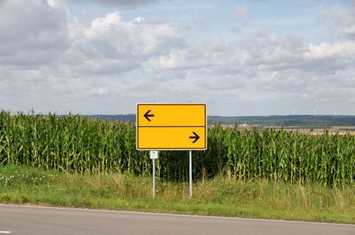 A yellow direction street sign pointing down a winding country road