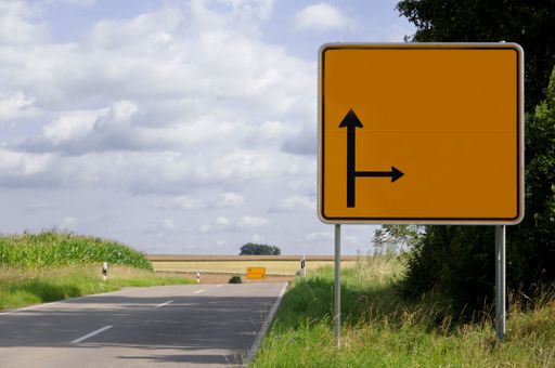 A yellow direction street sign pointing down a winding country road