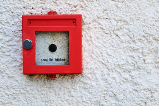 A high-resolution closeup of a manual red fire detector positioned on the side of a white wall