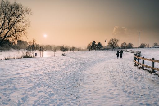 A long shot of two people walking on snow covered ground beside a wooden fence