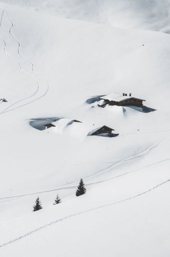 A beautiful winter scene of a snow-covered hillside with a small, wooden cabin tucked in the middle