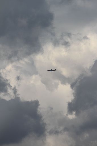A small airplane flying through a stormy sky, with majestic clouds visible in the background
