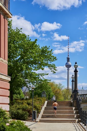 Berlin, Germany - April 26, 2020: View to a stairway near the river Spree with a sportsman from behind and the Berlin TV Tower in the background.