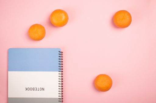 A top view of a notepad and tangerines on a pink background