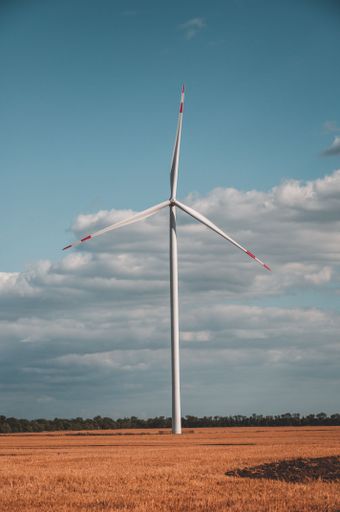 A modern wind turbine in a lush green field, illuminated by a bright blue sky